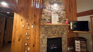 A cozy living room with a stone fireplace, wooden beams, and a television mounted on the wall.