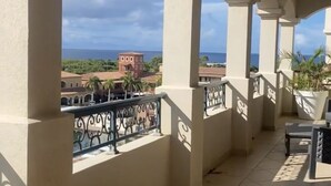 Un balcón con una mesa redonda y sillas, con vistas a una zona costera con edificios y palmeras.