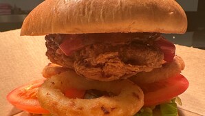 A sandwich with a bun, lettuce, tomato, onion rings, fried chicken, and a slice of meat. - Cozy Affordable Place in Great Yarmouth (Great Yarmouth)