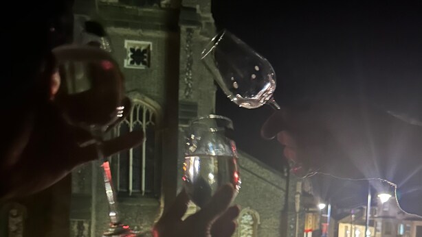 A person holding a glass with a reflective surface, a clock tower in the background, and a street with buildings. - Cozy Affordable Place in Great Yarmouth (Great Yarmouth)