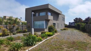 Een modern herenhuis met garage, omgeven door een grindpad en een aangelegde tuin met diverse planten.