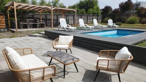 Een terras buiten met een zwembad, rieten meubels en een pergola.
