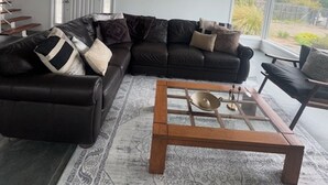 Een moderne woonkamer met een hoekbank, een glazen salontafel en een groot raam met uitzicht op het landschap.