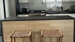 Een moderne keuken met witte kasten, een zwart aanrecht en een centraal eiland met twee houten krukken.