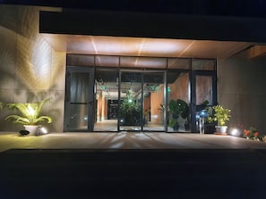 Une entrée moderne, avec des portes en verre, des plantes en pot et un sol en béton.