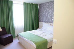 Une chambre d’hôtel avec un lit, des rideaux verts, une chaise et un papier peint à motifs.