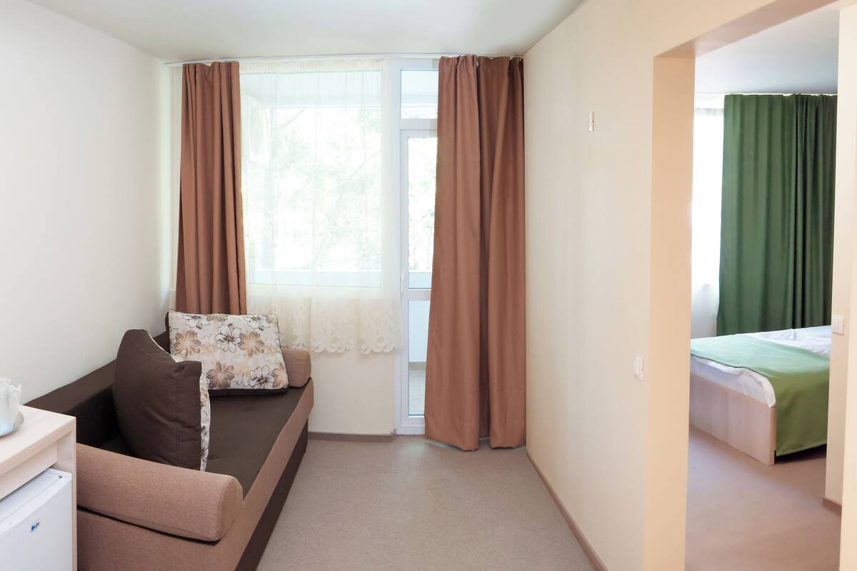 A room with a bed, a sofa, a small desk, and a window with curtains.