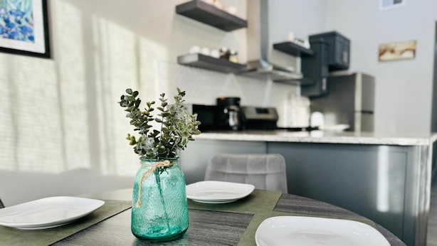 A dining table with a green placemat, a glass vase with green foliage, and white plates.
