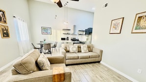 A modern living room with two sofas, a dining table, and a kitchen in the background.