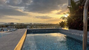 Ein Pool auf dem Dach mit Mosaikfliesen und Blick auf die Skyline bei Sonnenuntergang.