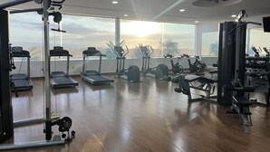 Ein geräumiger Fitnessraum mit unterschiedlichen Trainingsgeräten, großen Fenstern und Blick zum Himmel.
