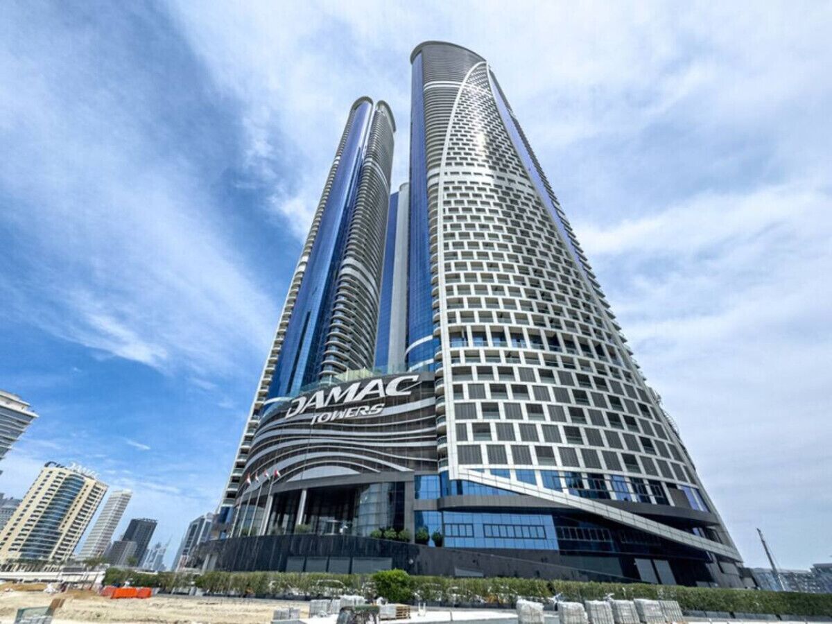 A modern high-rise building with a curved facade and the name "DAMAC TOWERS" prominently displayed.
