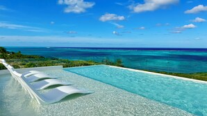 Un ciel d’un bleu éclatant, une piscine bordée de chaises longues blanches et une vue sur l’océan.