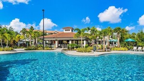 A swimming pool with a clear blue water surface, surrounded by palm trees and a building with a tiled roof. - Orlando Resort Rentals Near Universal (Orlando)