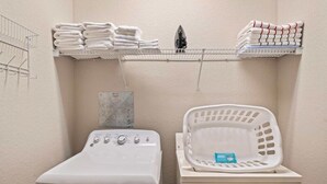 A laundry area with a washing machine, a dryer, and shelves with folded towels. - Orlando Resort Rentals Near Universal (Orlando)