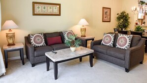 A living room with two sofas, a coffee table, and two lamps. There are framed pictures on the walls and a chandelier above the dining table. - Orlando Resort Rentals Near Universal (Orlando)