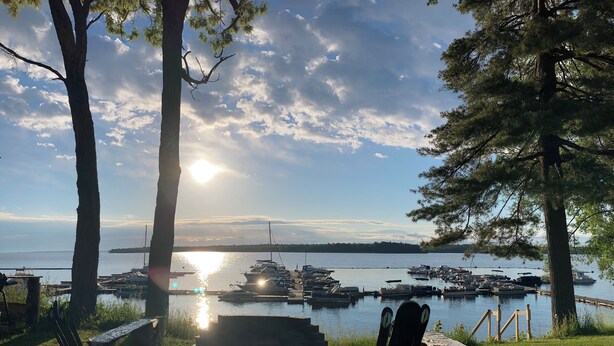 A lakeside view with docked boats, a wooden deck, and two Adirondack chairs.