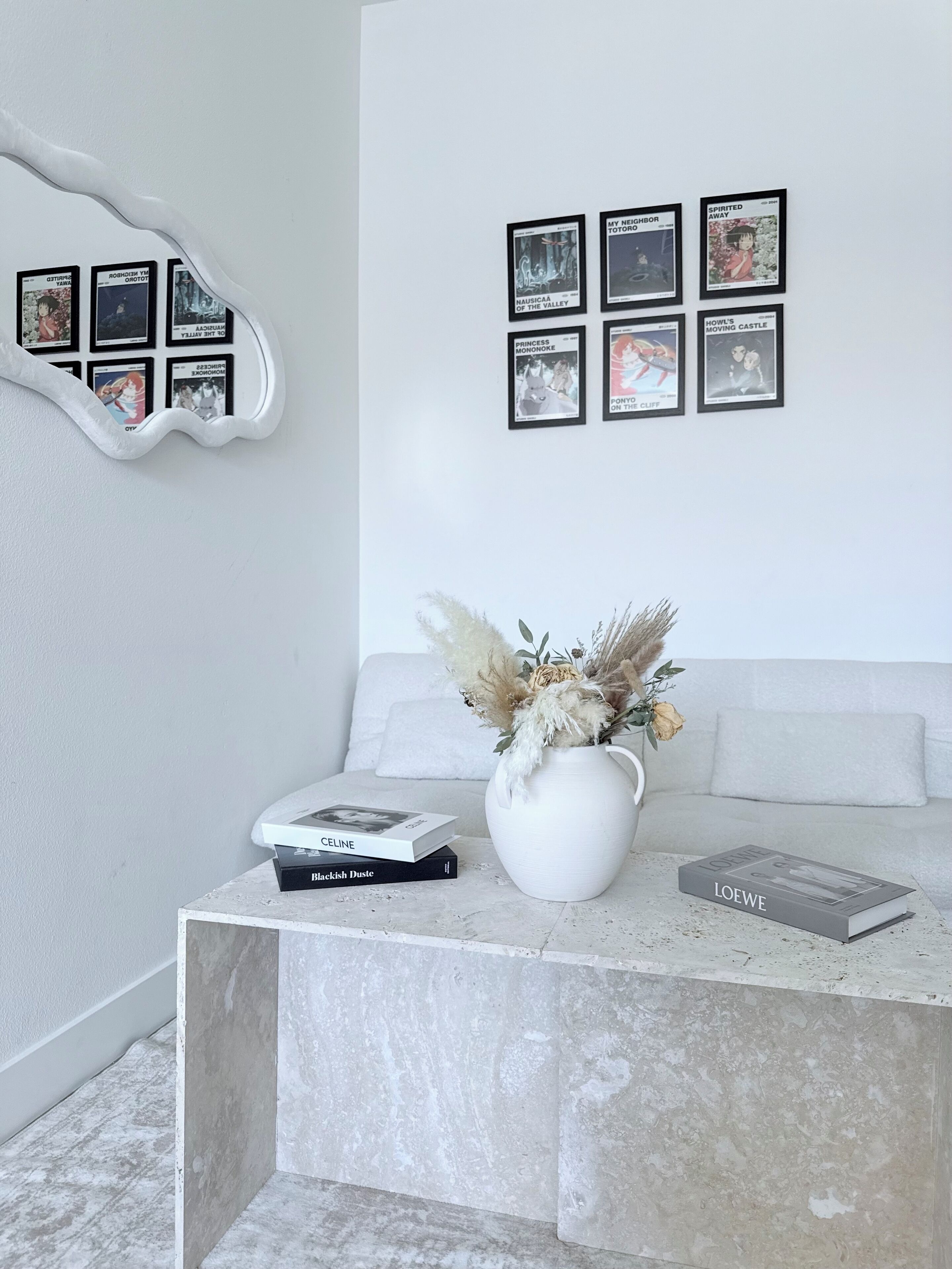 Una sala moderna con una mesa de centro de mármol, un jarrón con flores secas y una selección de libros.