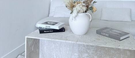 Una sala moderna con una mesa de centro de mármol, un jarrón con flores secas y una selección de libros.