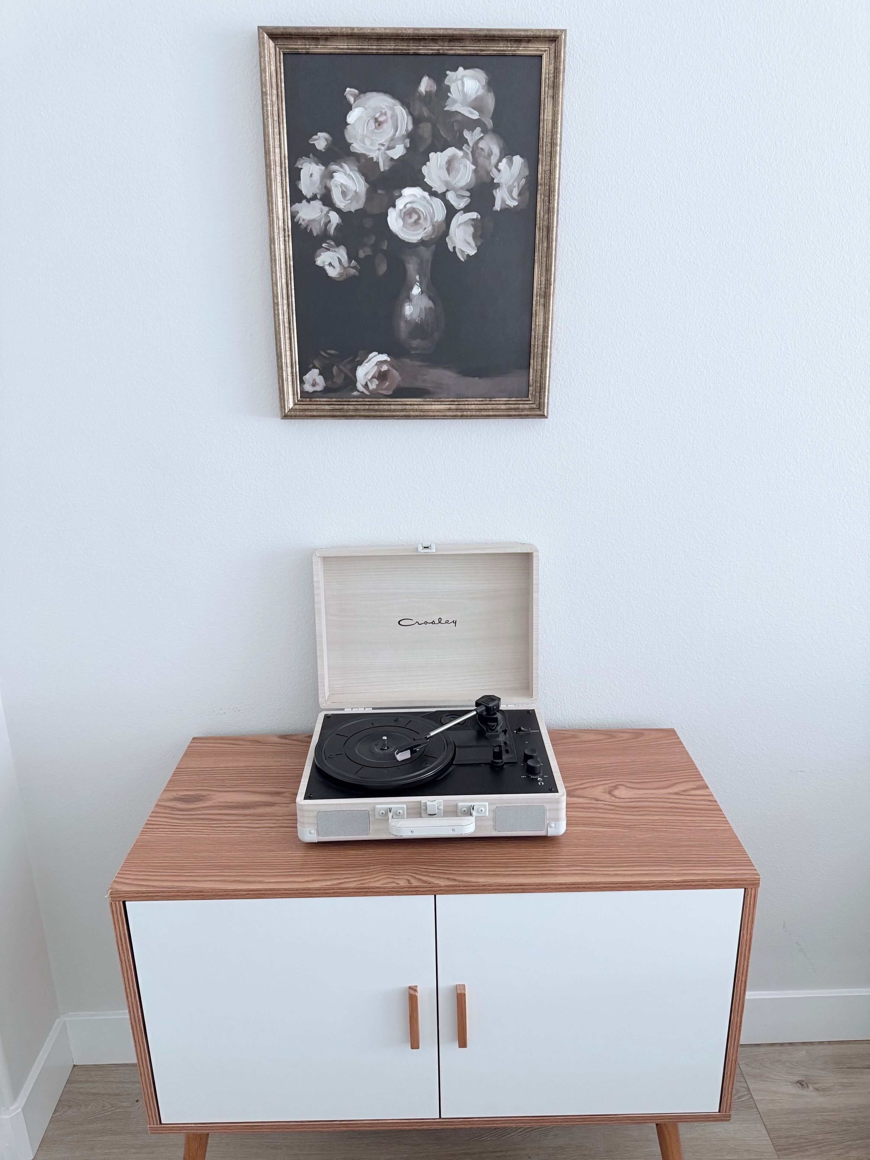 A wooden cabinet with a record player on top, a framed painting above it, and a wooden box with the word "Croakey" on it.