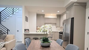 A modern kitchen with a wooden dining table, grey cabinets, and a stainless steel refrigerator.