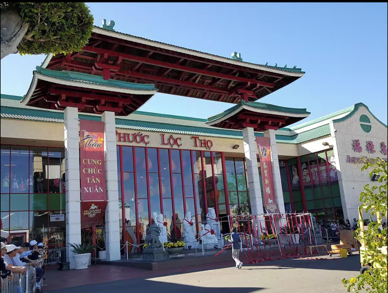 A traditional building with a red roof and large windows, featuring statues and banners.