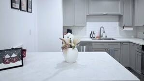 A modern kitchen with white cabinets, a white countertop, and a vase with dried plants.