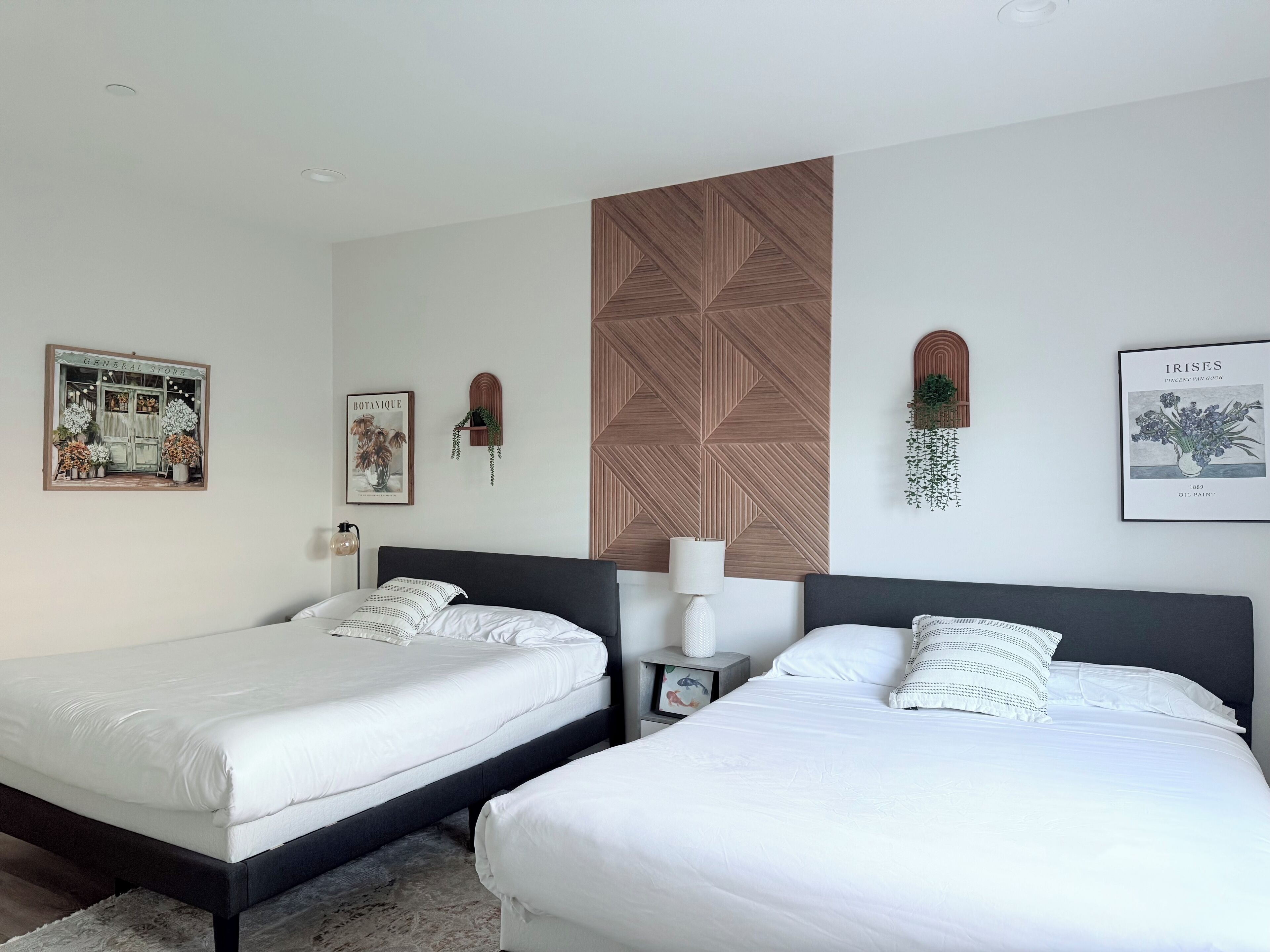 A bedroom with two beds, a wooden accent wall, and wall-mounted plants.