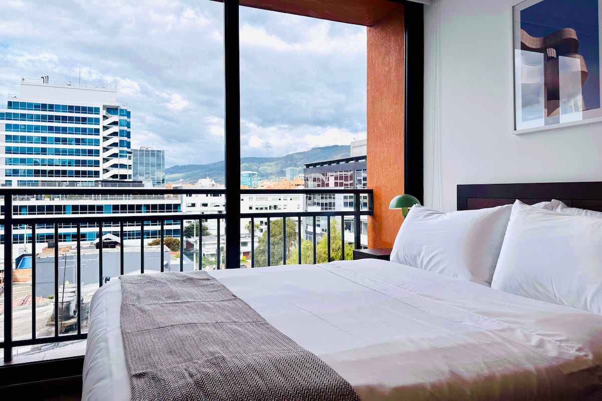 A hotel room with a large bed, a view of the cityscape, and a balcony.