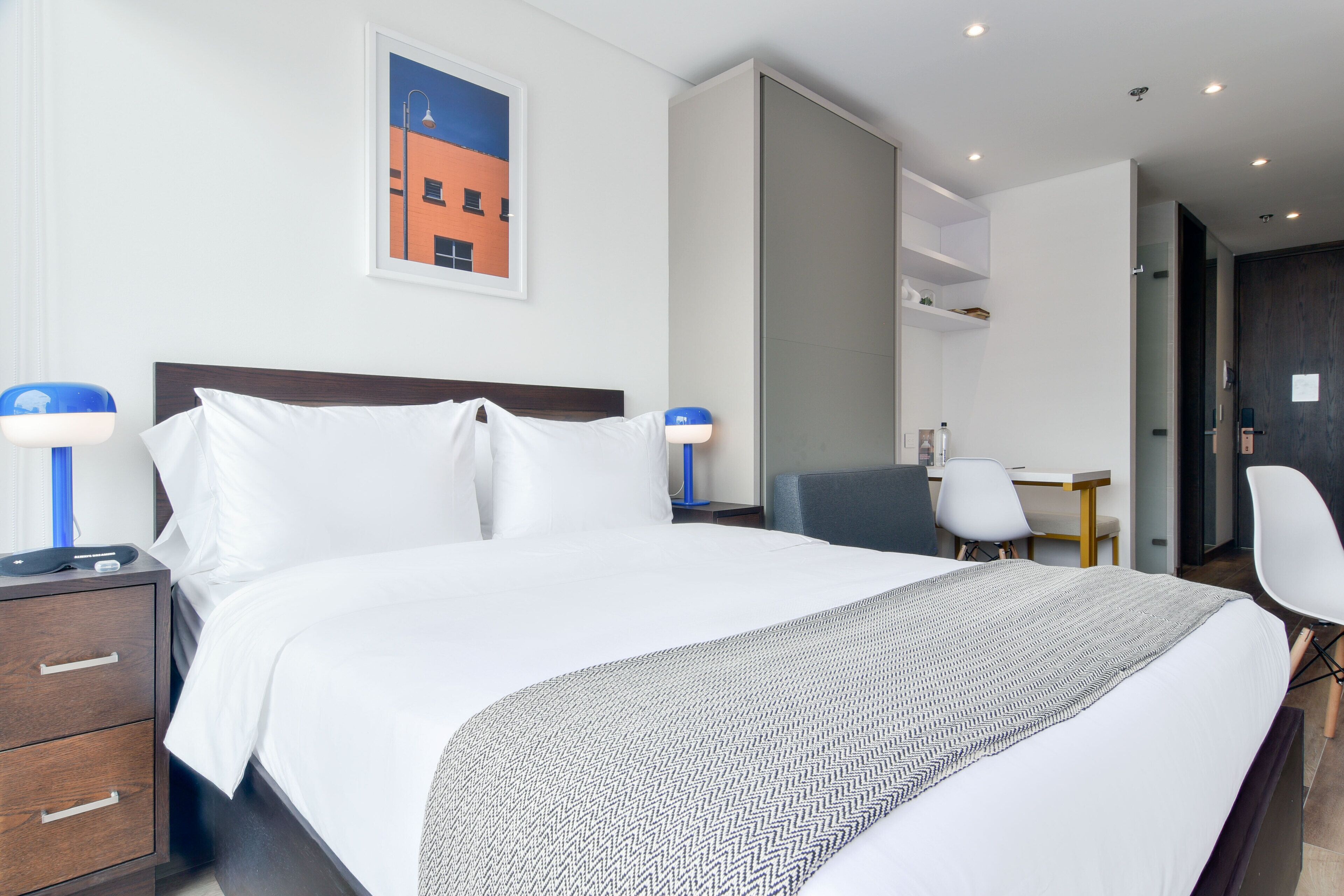 A hotel room with a large bed, two bedside tables with lamps, a desk, and a chair.