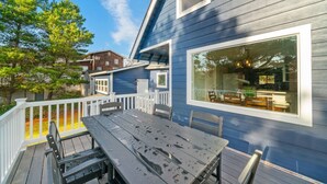 A deck with a table and chairs, a large window, and a blue house.