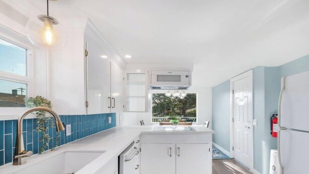 A modern kitchen with white cabinets, a blue backsplash, and a large island.