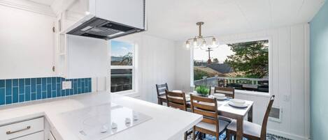 A modern kitchen with white cabinetry, a built-in stove, and a dining area with wooden chairs and a blue patterned rug.