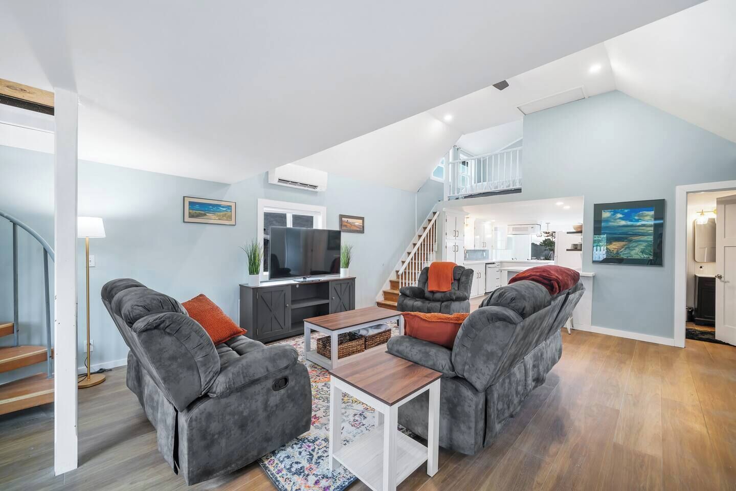 A modern living room with grey sofas, a coffee table, and a TV. There is a staircase leading to an upper level.