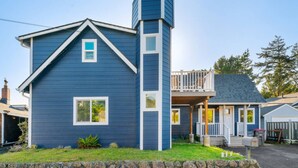 A two-story house with a prominent tower-like structure on the right side, a front porch, and a small deck.