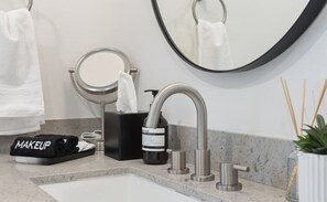 A bathroom with a sink, a mirror, a towel, a makeup bag, and a plant. - Beltline Lux Loft (Atlanta)