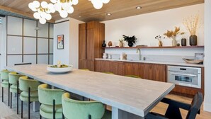 A modern kitchen with a long island, green bar stools, wooden cabinets, and pendant lighting. - Beltline Lux Loft (Atlanta)