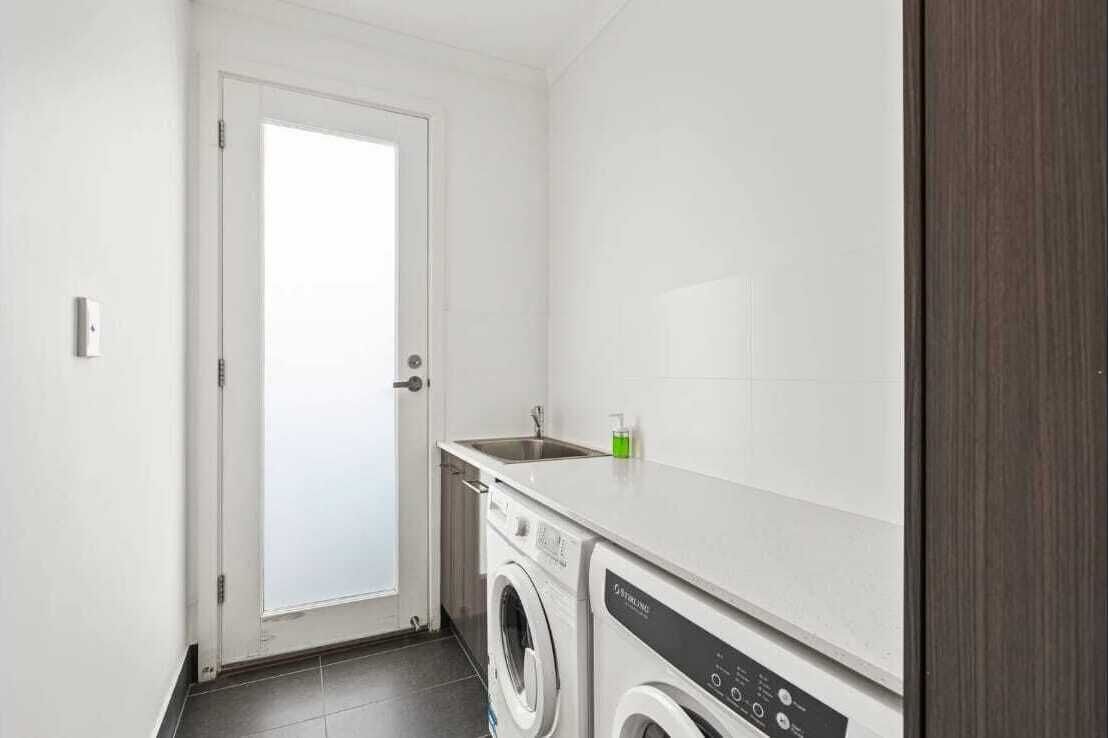 A compact laundry room with a washing machine, a sink, and a door.