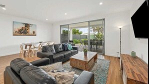 A modern living room with a black leather sofa, a wooden coffee table, and a dining area with a white table and chairs.