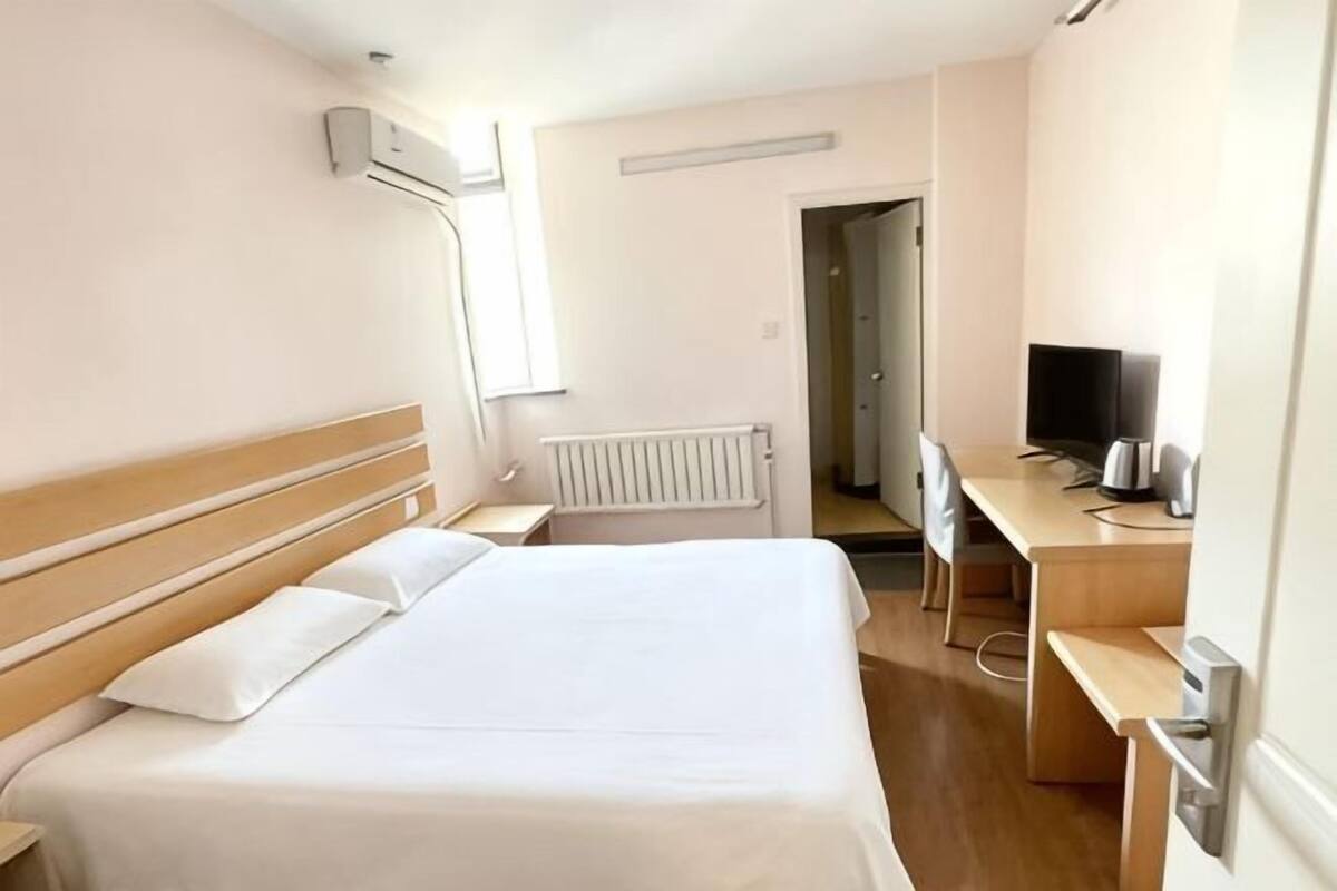 A hotel room with a bed, a desk with a computer, a TV, and a radiator.