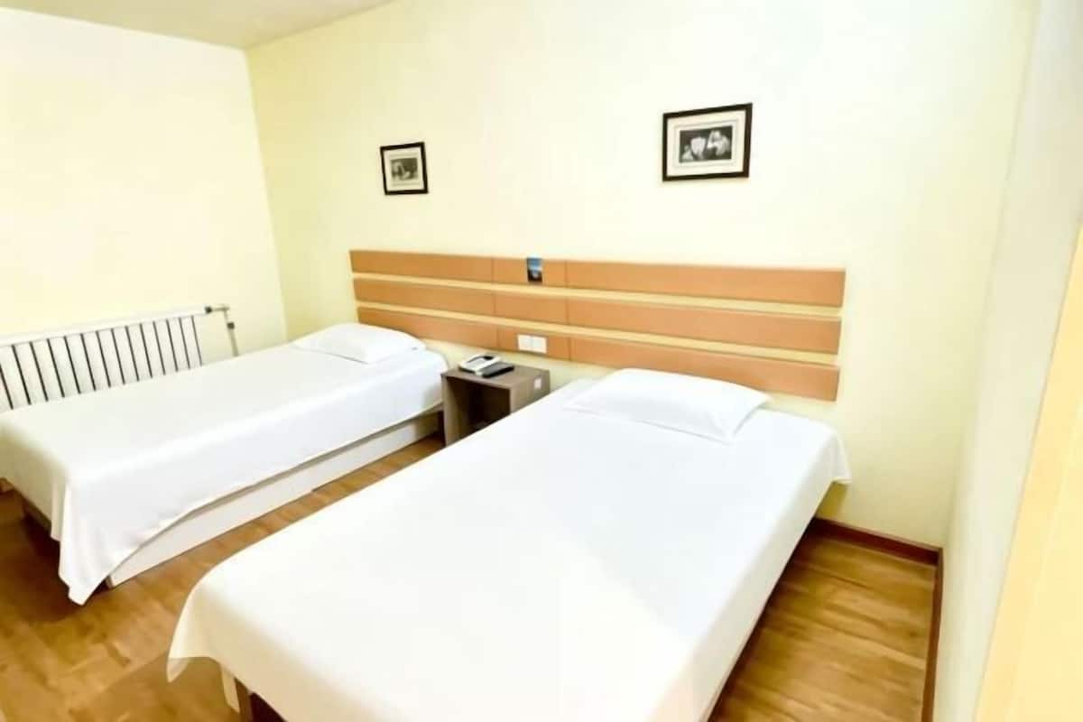 A hotel room with two single beds, a wooden headboard, a bedside table with a lamp, and a wall-mounted picture.