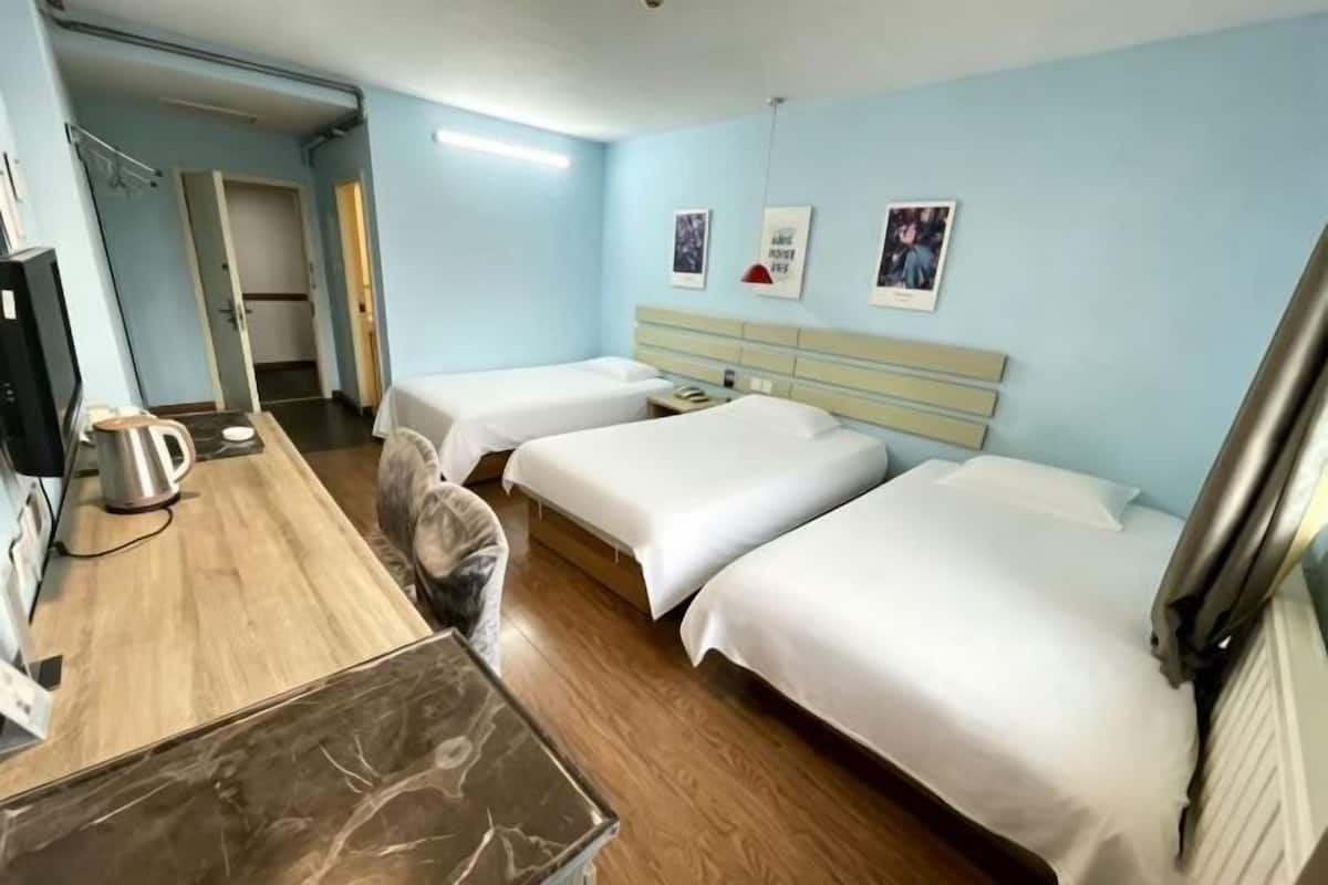 A hotel room with two beds, a desk with a kettle, a chair, and a television.