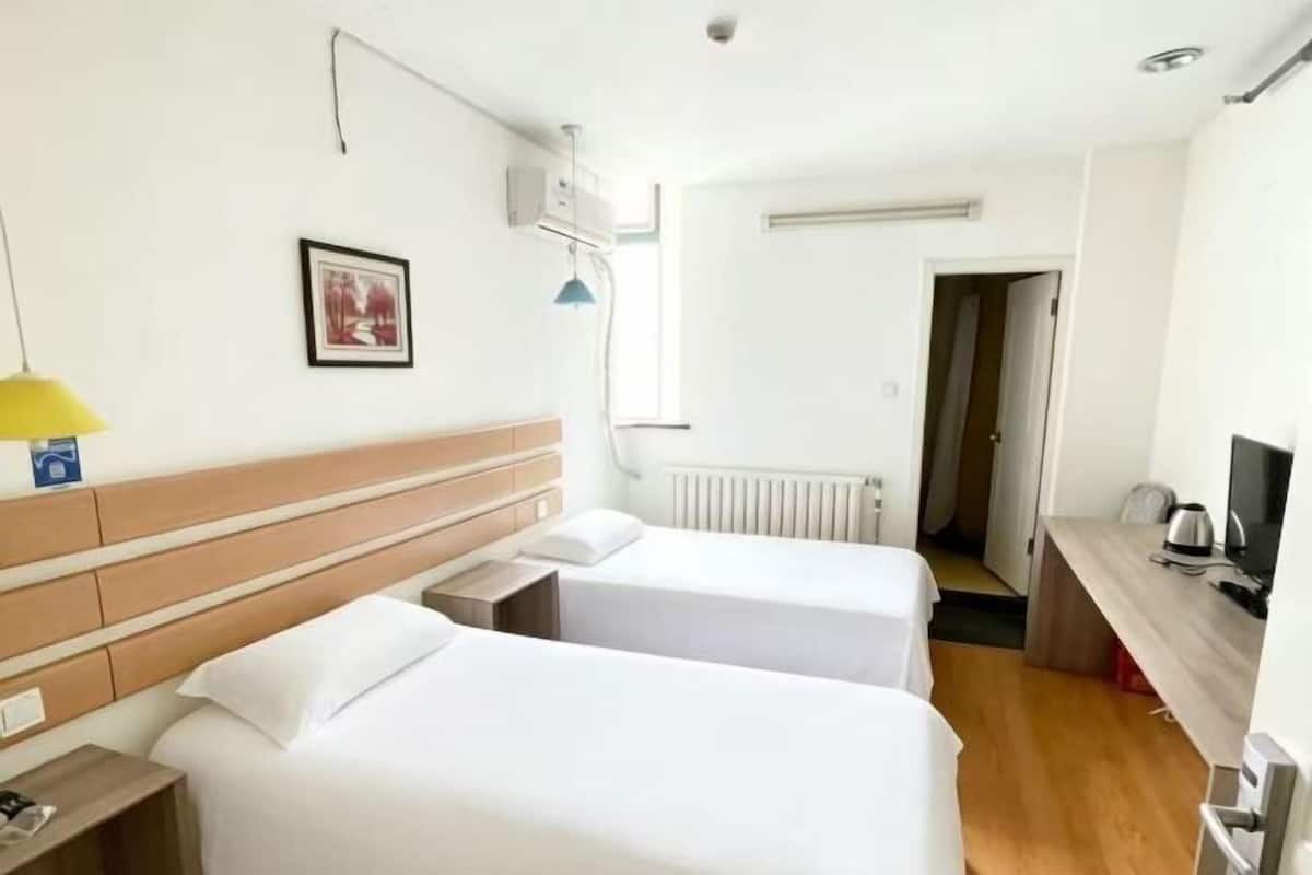 A hotel room with two beds, a desk with a TV, a lamp, and a picture on the wall.