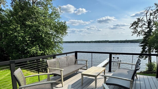 A deck with outdoor furniture, a view of a lake, and a grassy area.