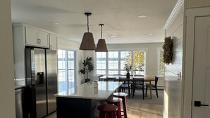 A modern kitchen with a central island, bar stools, and a dining area with a view of the outdoors.