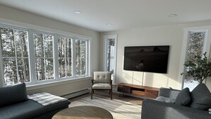 A modern living room with a large window, a sofa, a chair, a coffee table, and a flat-screen TV.