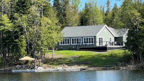 A lakeside cabin with a large deck and a covered outdoor seating area.