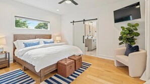 Une chambre moderne avec un grand lit, un ventilateur de plafond, une télévision et une vue sur la salle de bain.