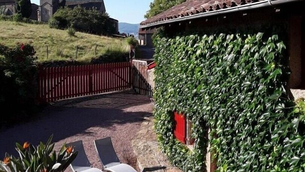 A courtyard with a wooden table and chairs, a red fence, and a building with ivy-covered walls. - La Rose des Vents - JALOGNY (JALOGNY)