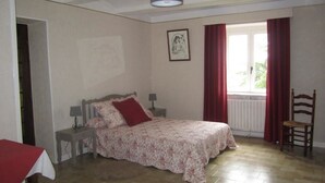 A bedroom with a bed, a chair, a nightstand, a lamp, a window with curtains, and a framed picture on the wall. - La Rose des Vents - JALOGNY (JALOGNY)